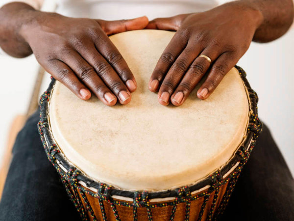 A djembe drum showing the rope crown with two hands resting on the skin