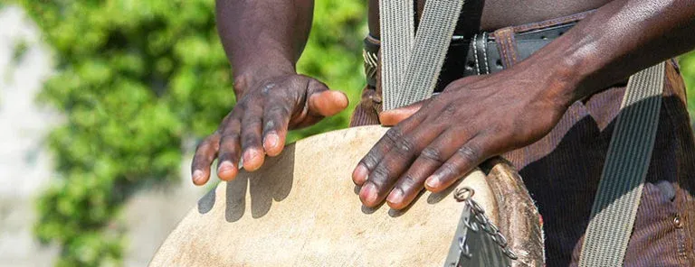 A pair of hands on a djembe, playing the drum in the sun